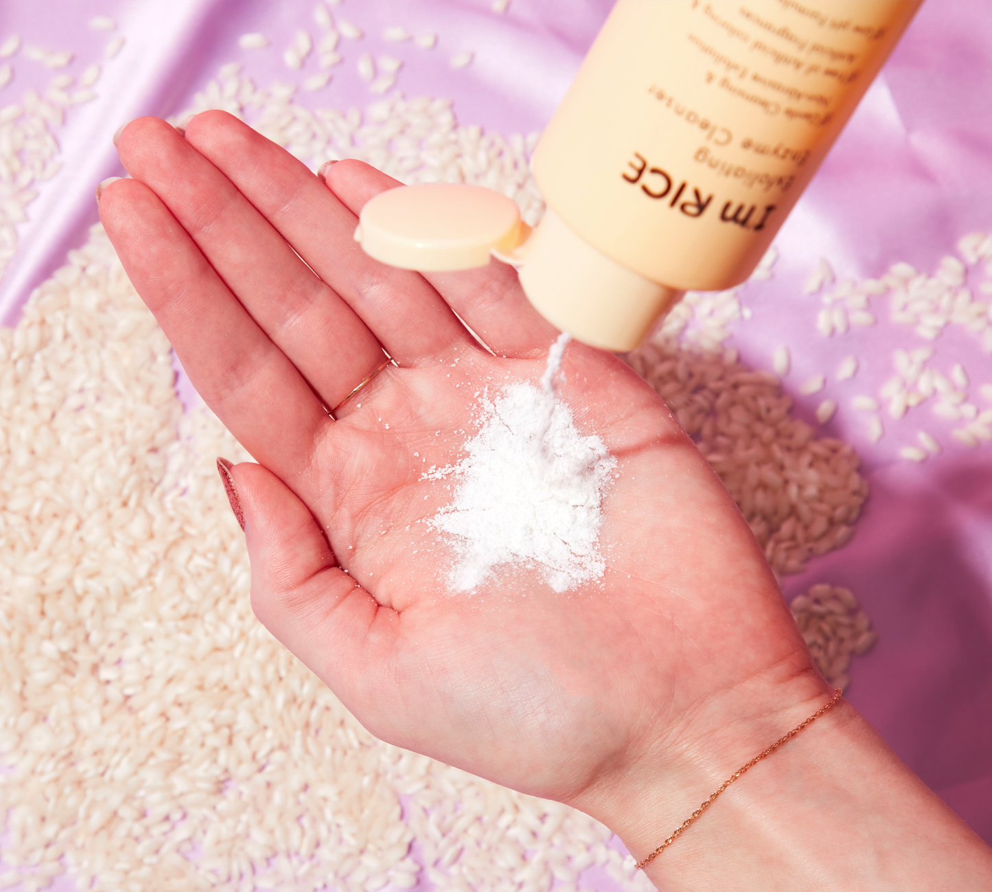 Hand holding a small amount of white powder with a bottle labeled 'RICE' in the background.