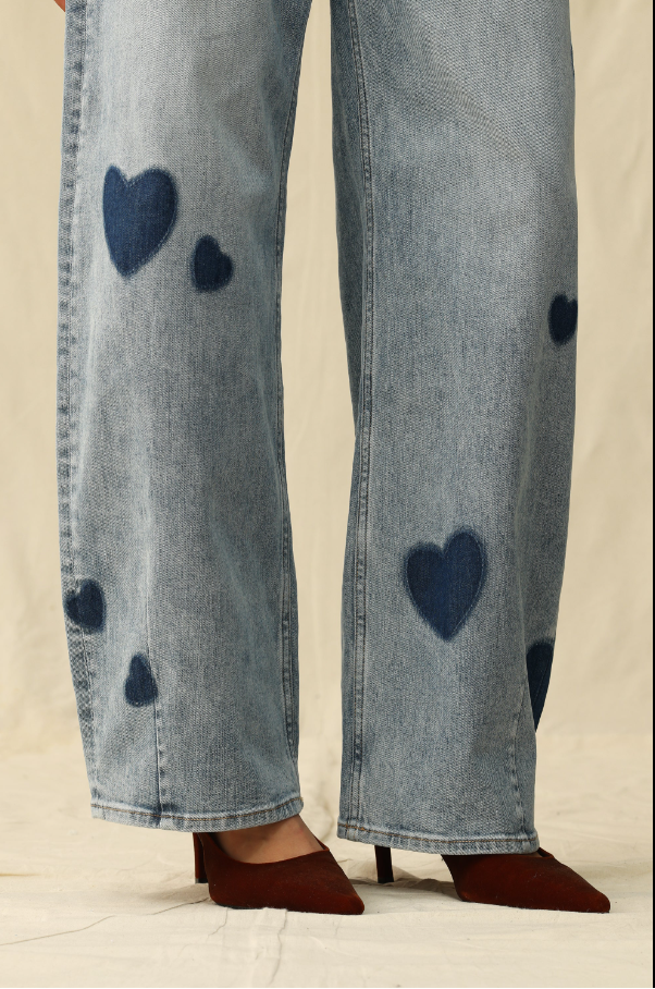 Blue jeans with heart patterns worn by a person on a neutral background