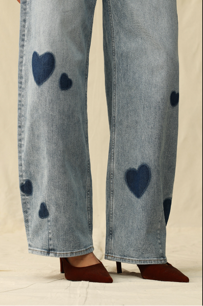 Blue jeans with heart patterns worn by a person on a neutral background