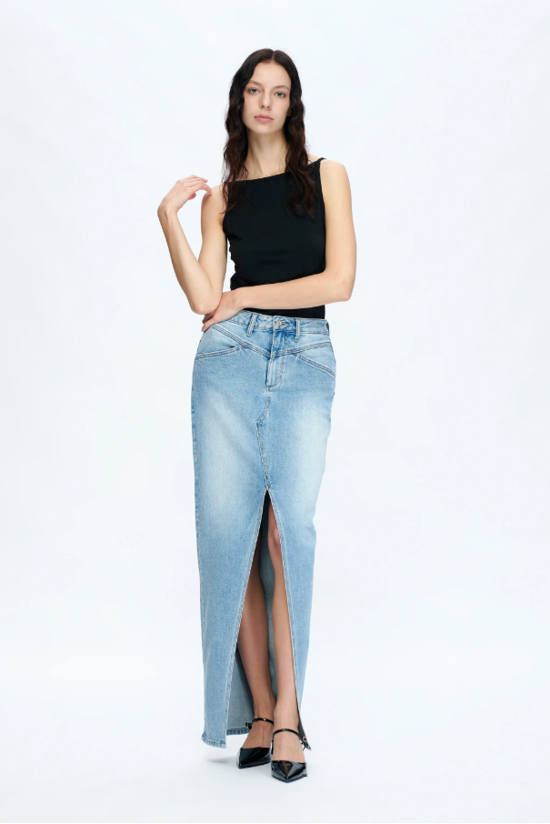 Woman wearing a black top and light blue denim skirt with a slit on a white background