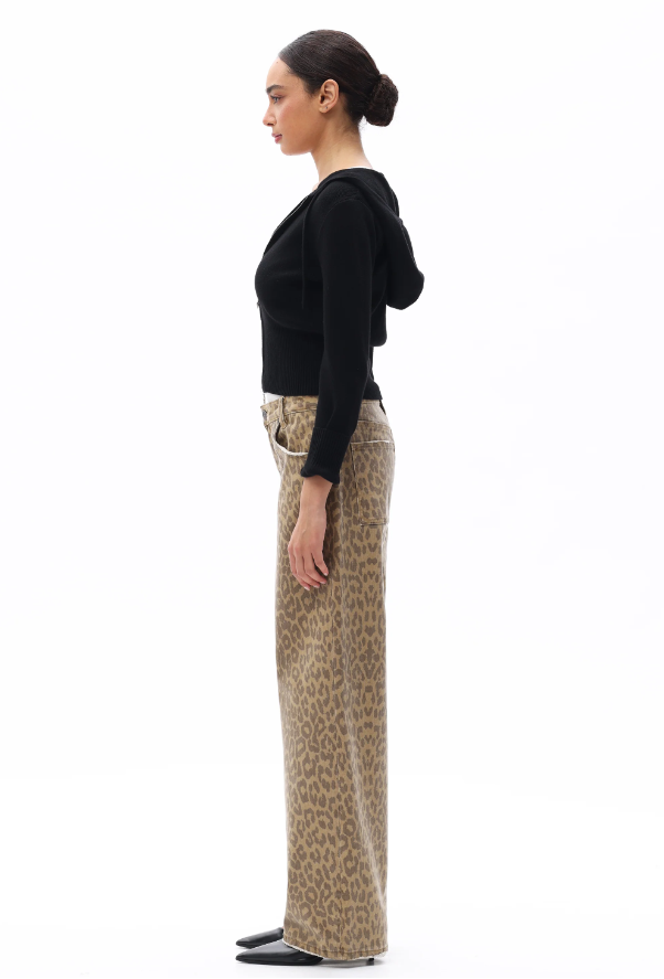 Woman wearing a black top and patterned pants standing against a white background