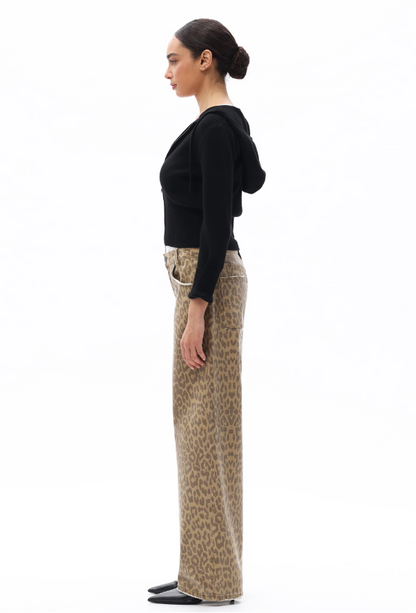 Woman wearing a black top and patterned pants standing against a white background
